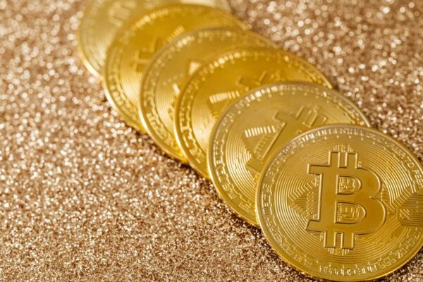 A stack of gold Bitcoin coins placed on a shimmering gold glitter background.