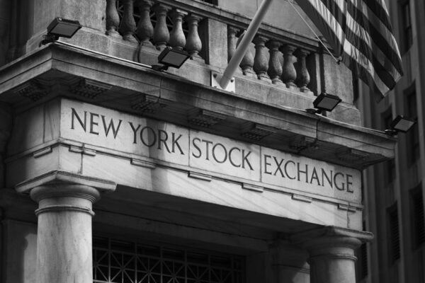 Black and white photo of the New York Stock Exchange facade with USA flag.