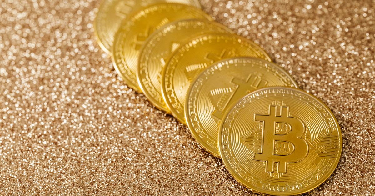 A stack of gold Bitcoin coins placed on a shimmering gold glitter background.