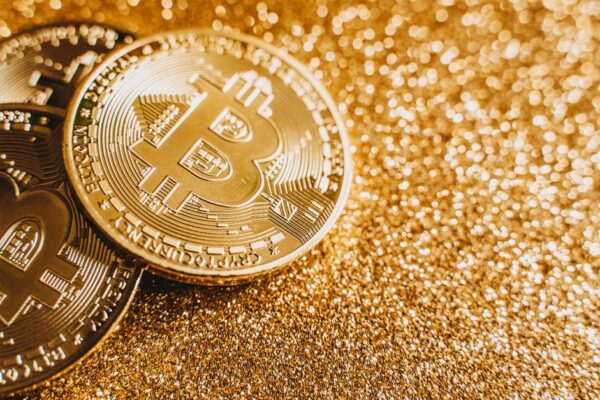 A close-up image of bitcoins placed on a sparkling gold glitter background, symbolizing cryptocurrency wealth.