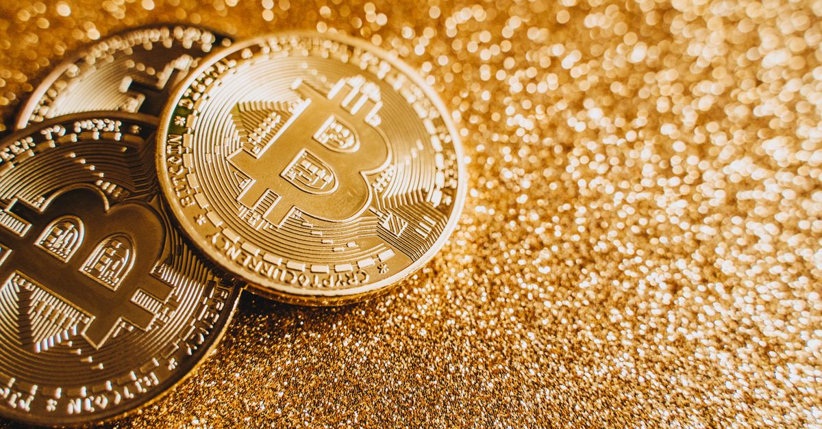 A close-up image of bitcoins placed on a sparkling gold glitter background, symbolizing cryptocurrency wealth.