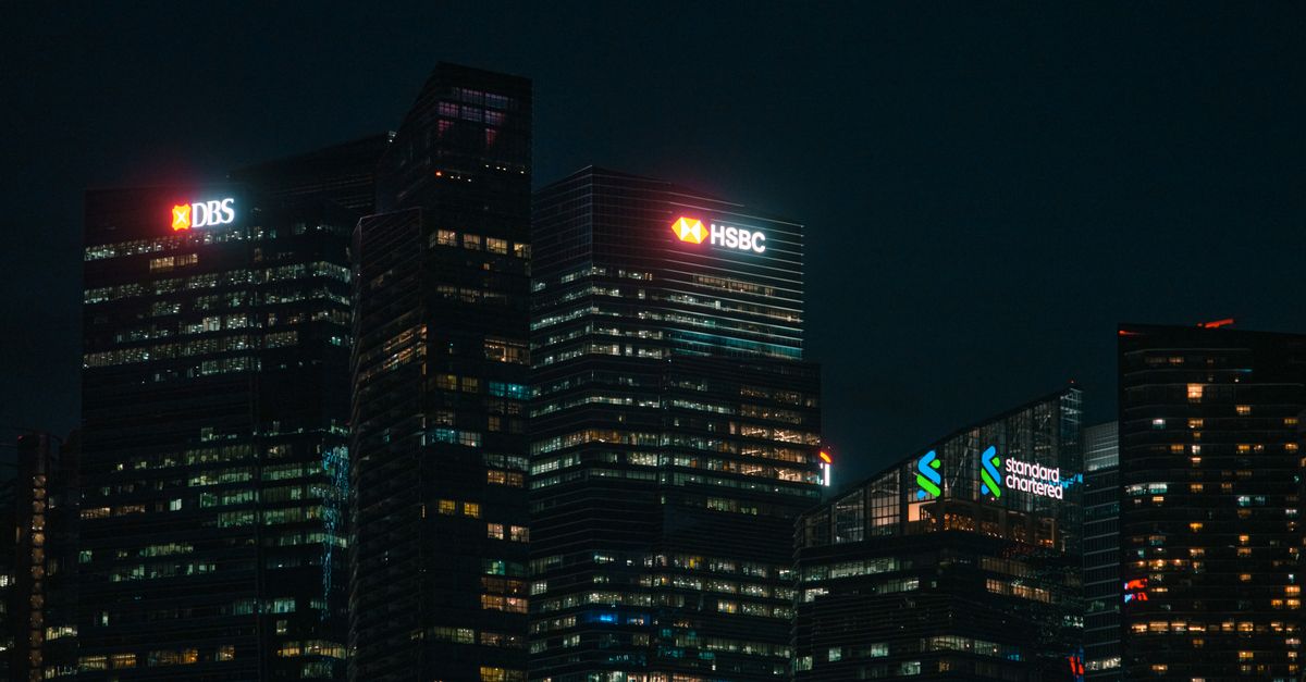 Illuminated city skyscrapers of major banks in Singapore's financial district at night.
