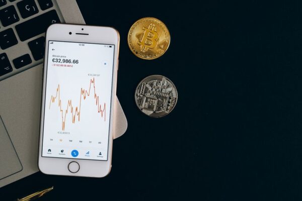 Smartphone displaying Bitcoin price chart alongside Bitcoin and Ethereum coins on black background.