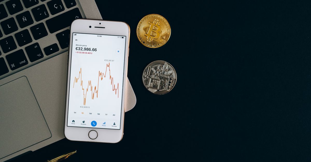 Smartphone displaying Bitcoin price chart alongside Bitcoin and Ethereum coins on black background.