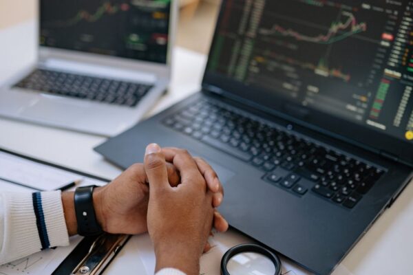 Man seated at a desk using laptops to monitor stock market trends and investments.