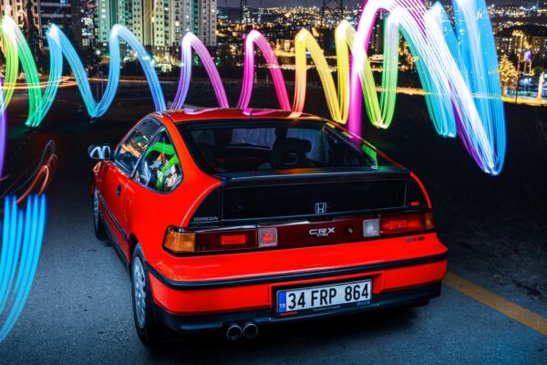 Red Honda CRX parked at night with colorful light trails in Ankara's cityscape.