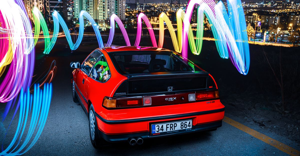 Red Honda CRX parked at night with colorful light trails in Ankara's cityscape.