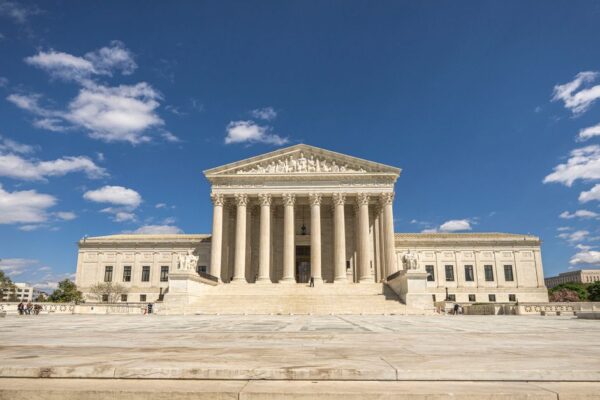 Front view of the United States Supreme Court building on a sunny day with blue sky and clouds.