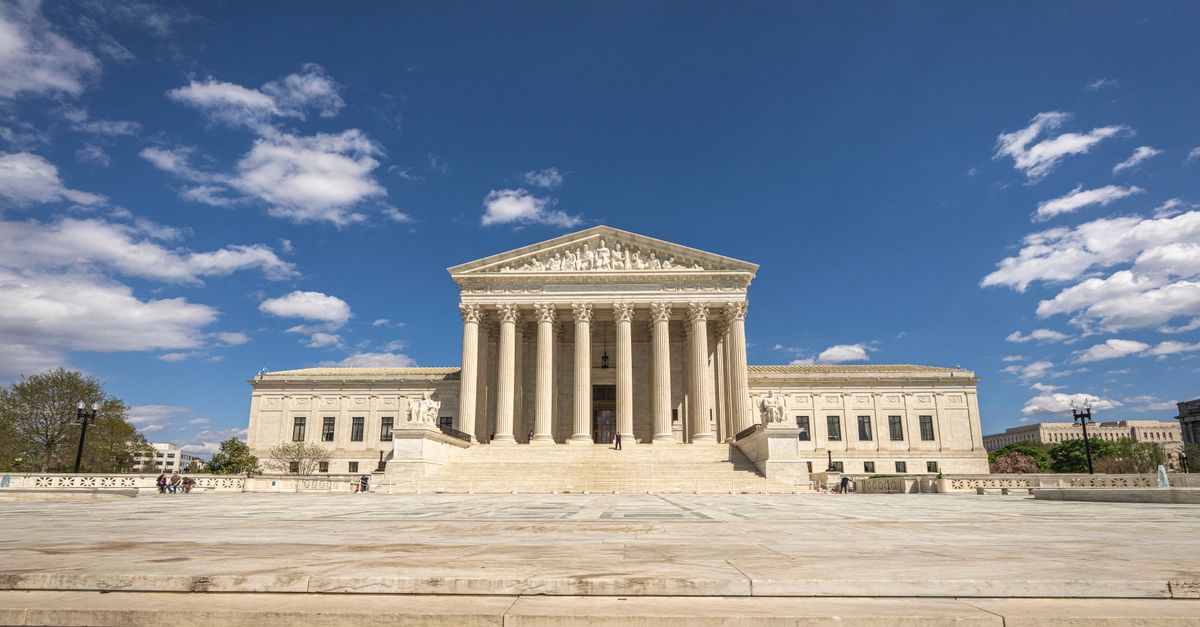 Front view of the United States Supreme Court building on a sunny day with blue sky and clouds.