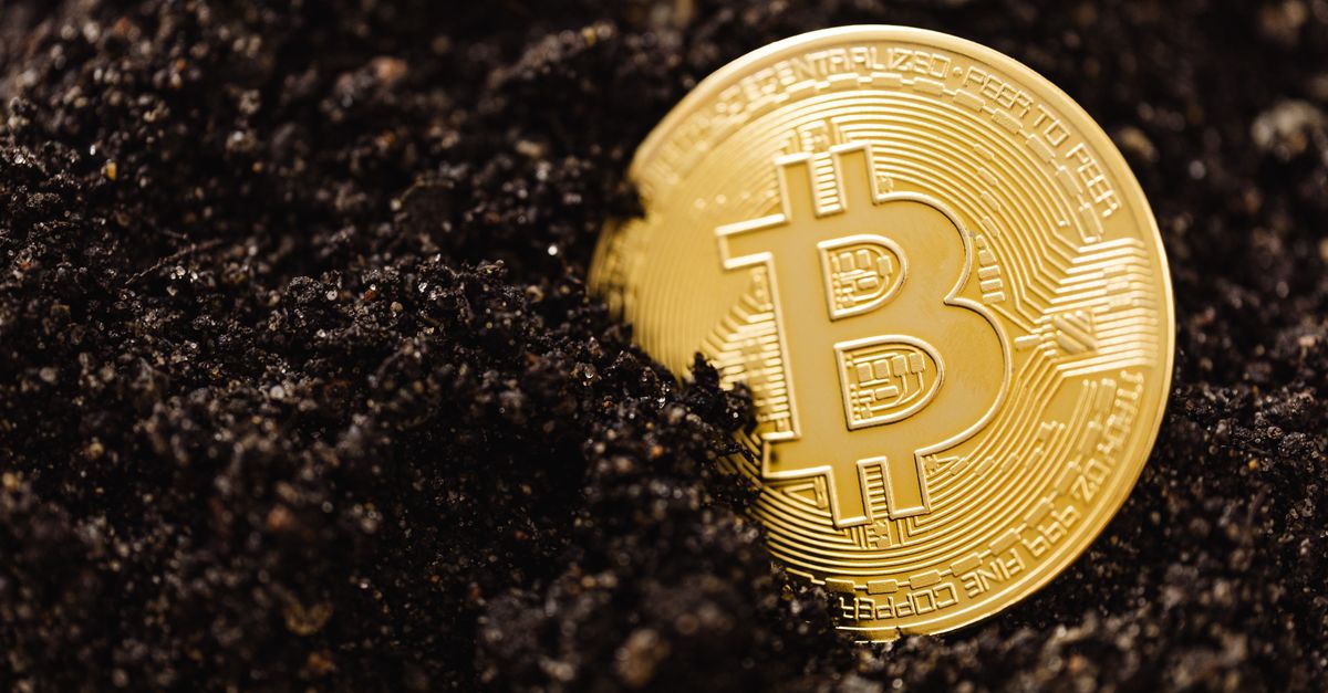 Close-up of a golden Bitcoin coin partially buried in soil, illustrating digital currency mining concept.