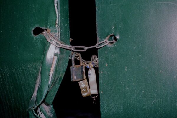 Close-up of a rusty padlock and chain securing green metal doors, blocking entry.