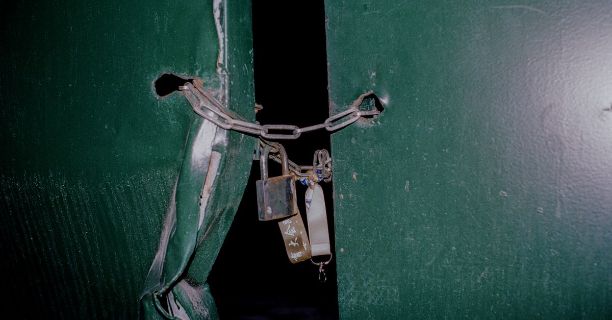 Close-up of a rusty padlock and chain securing green metal doors, blocking entry.