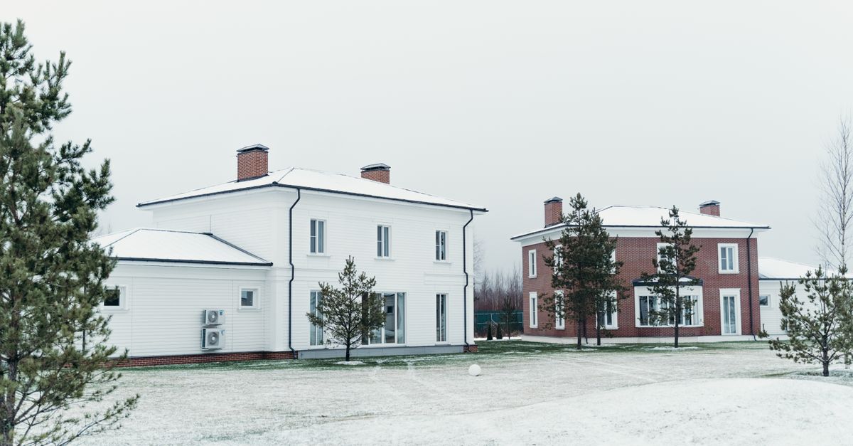 Two modern houses in a snowy winter scene with pine trees.