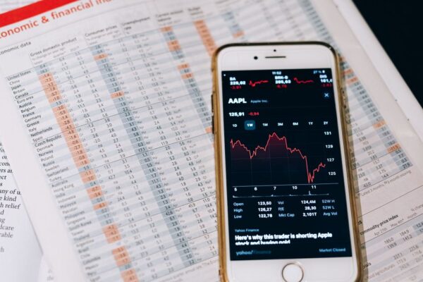 Smartphone displaying stock market data on papers with financial charts.